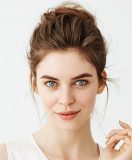 Portrait of young beautiful playful girl with bun looking at camera posing over white background. Copy space.